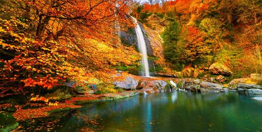 Waterfall surrounded by red and yellow autumn trees.
